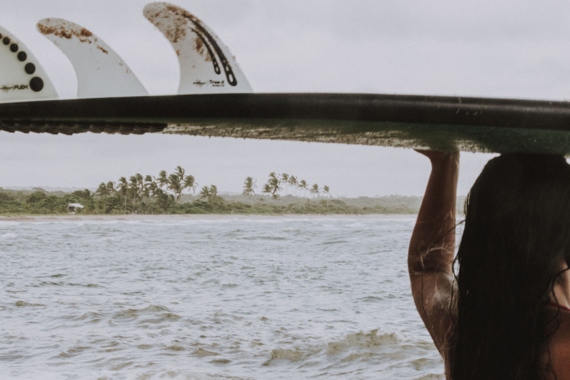 A surfer carrying a board beside the coast of Bahia